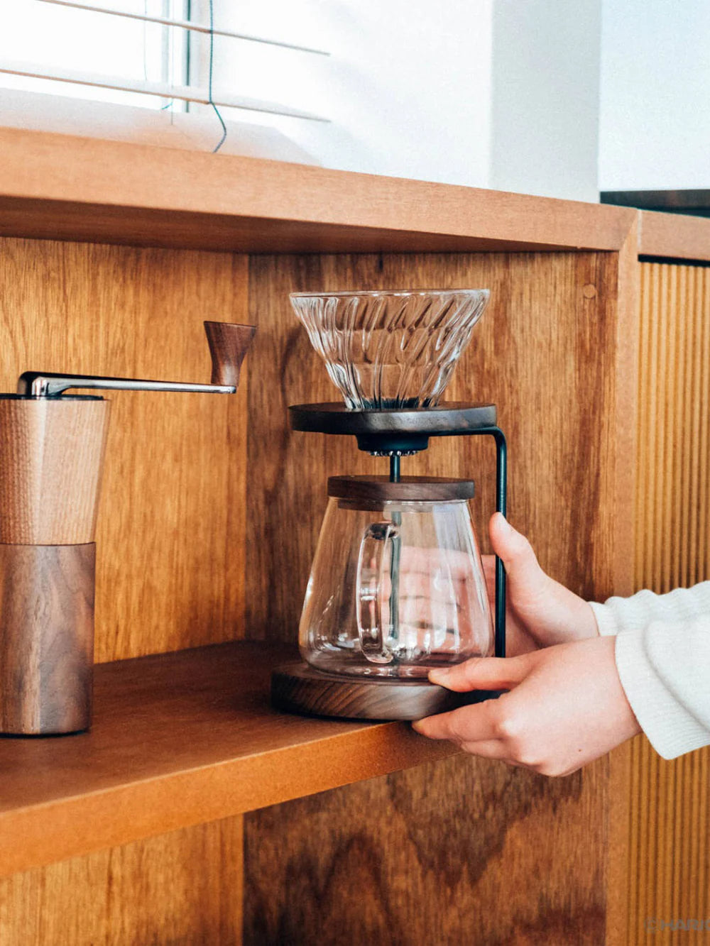Hand holding a glass coffee maker on a wooden shelf