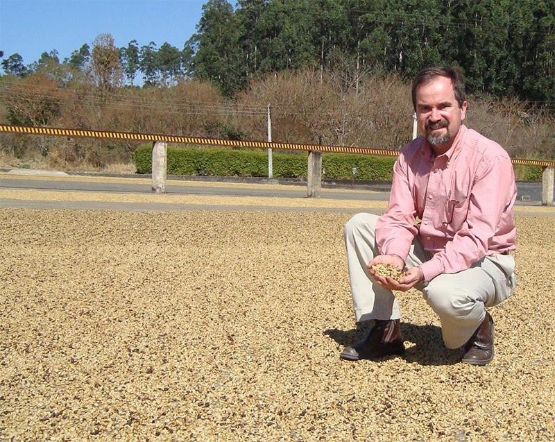 Gabriel Carvahlo Dias squatting on the farm's patio, showing us his sun-dried coffee.