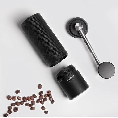 Disassembled black coffee grinder showing the coffee container, handle,  and beans on a light gray background