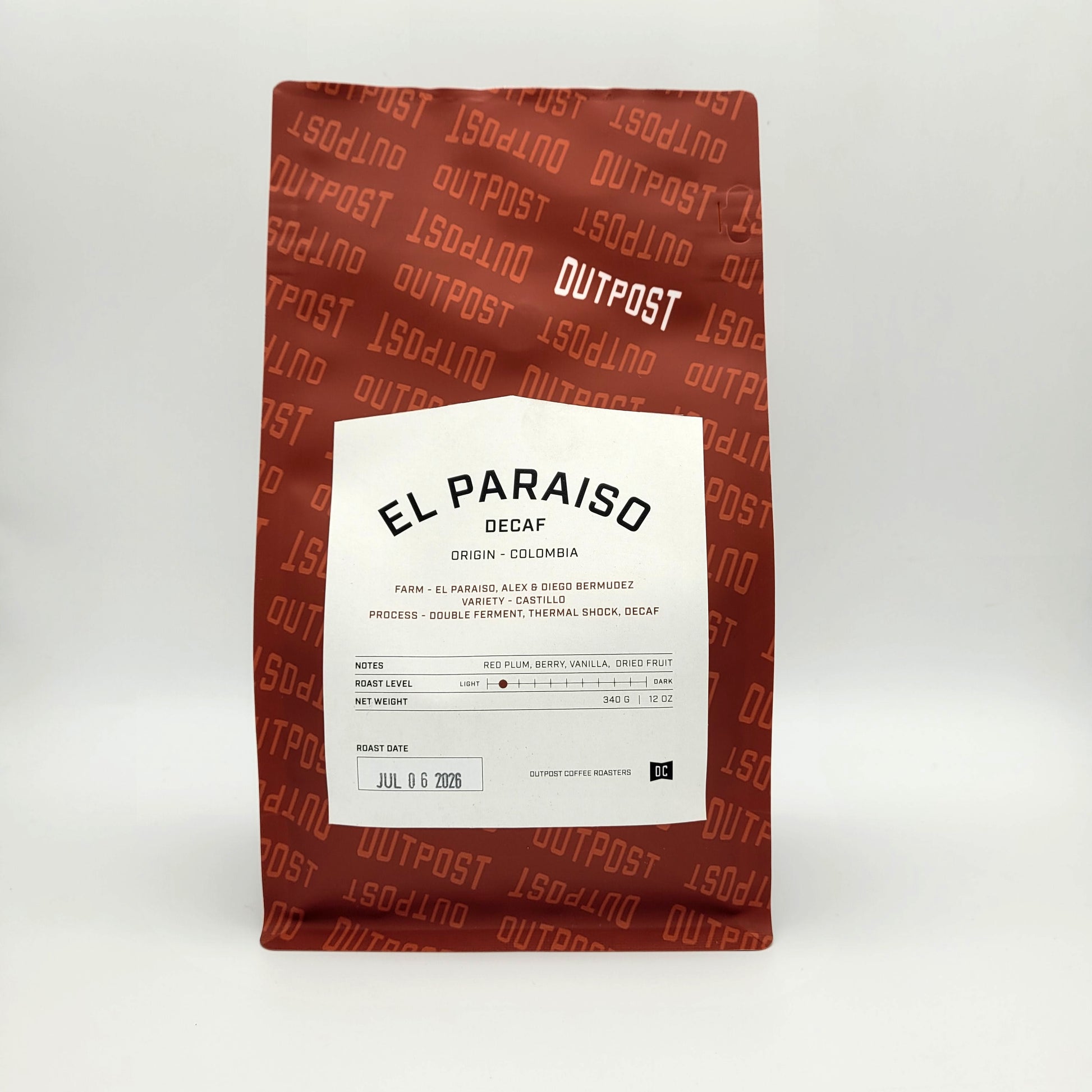 A bag of Outpost El Paraiso Decaf coffee on a light gray background. The bag is a reddish-brown color with a repeating 'OUTPOST' pattern and features a large white label in the center with black text.